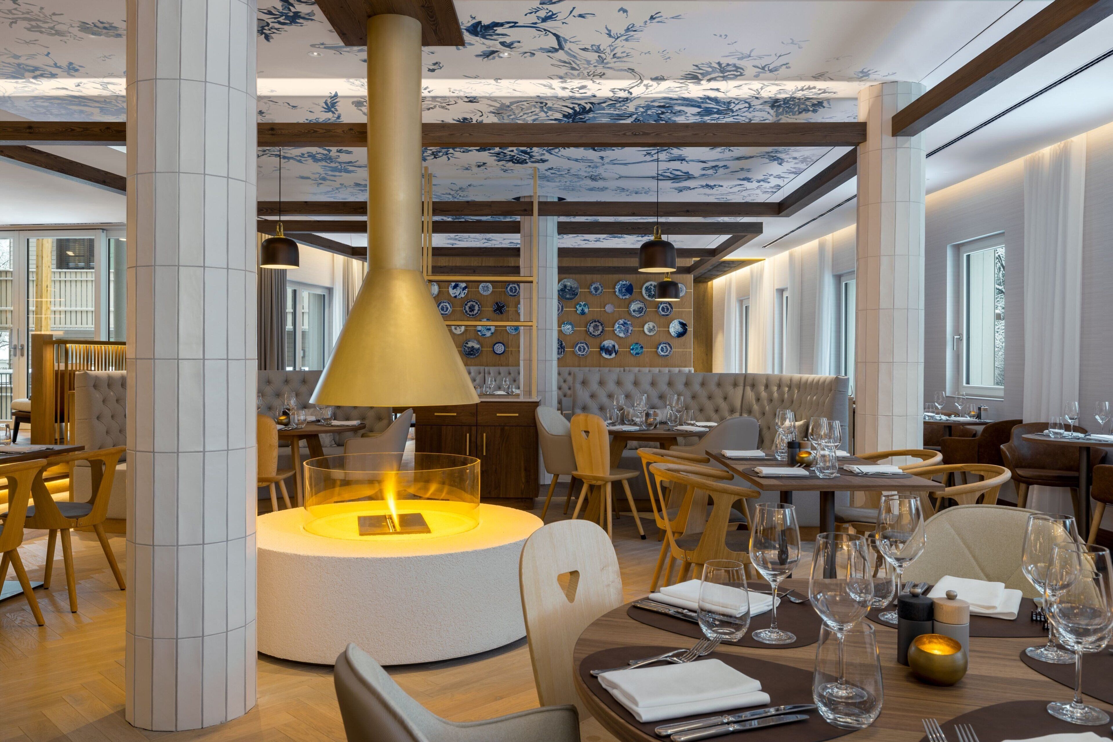 A modern dining area with a central round table, wooden beams, and a decorative ceiling.