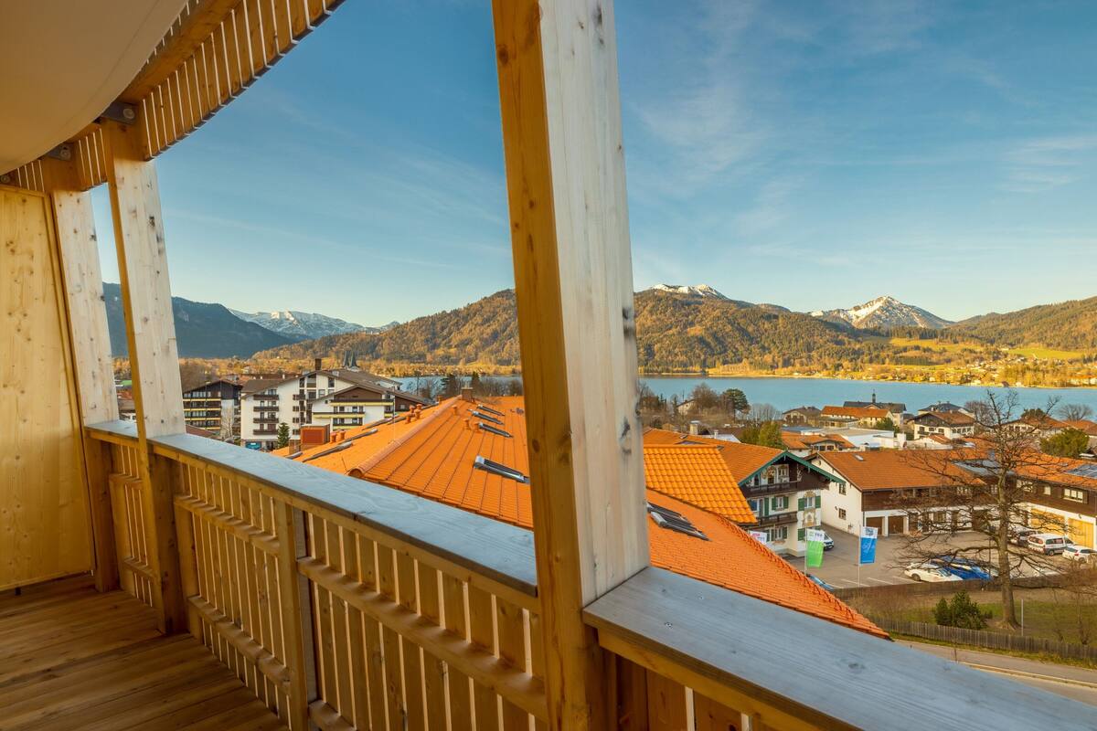 A wooden balcony with a view of a town, mountains, and a lake.