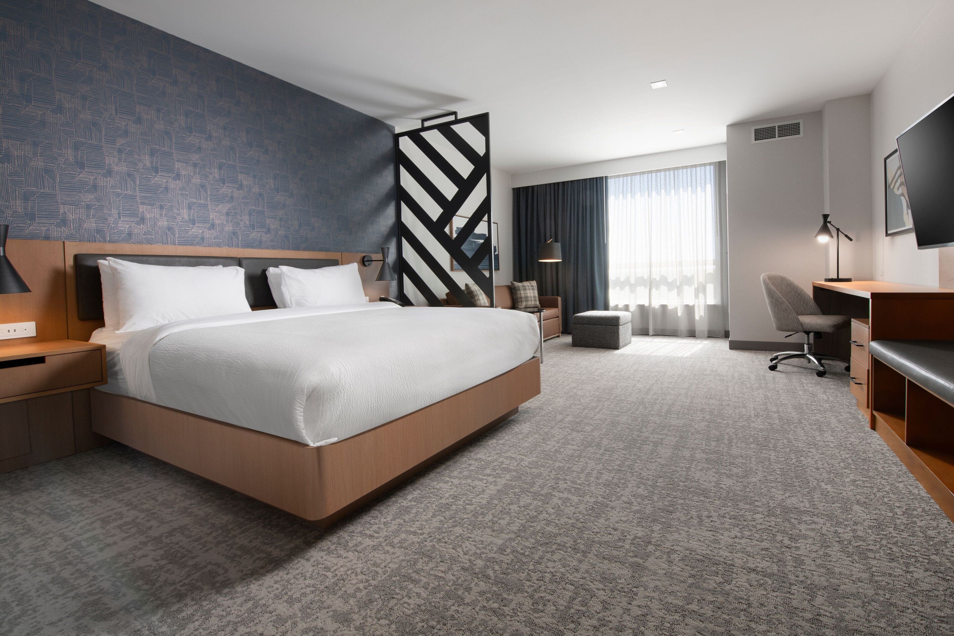 Una habitación de hotel moderna con una cama grande, un escritorio y un televisor.