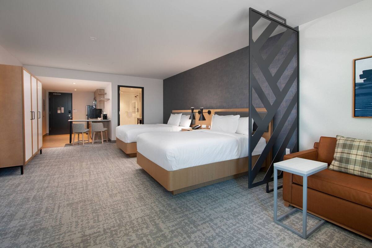 A modern hotel room with a large bed, a desk, a sofa, and a view of the city.
