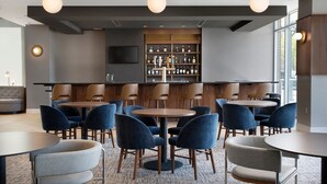 Un espace bar moderne avec des tables rondes et des chaises bleues, un comptoir en bois et un téléviseur fixé au mur.