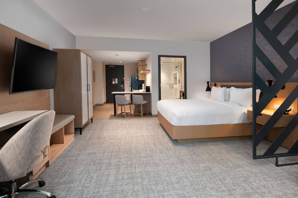 A modern hotel room with a bed, desk, chair, and a TV.