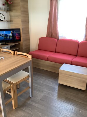 A modern living room with a wooden dining table, a red sofa, and a television on a stand. - Luxury mobile home (Fréjus)