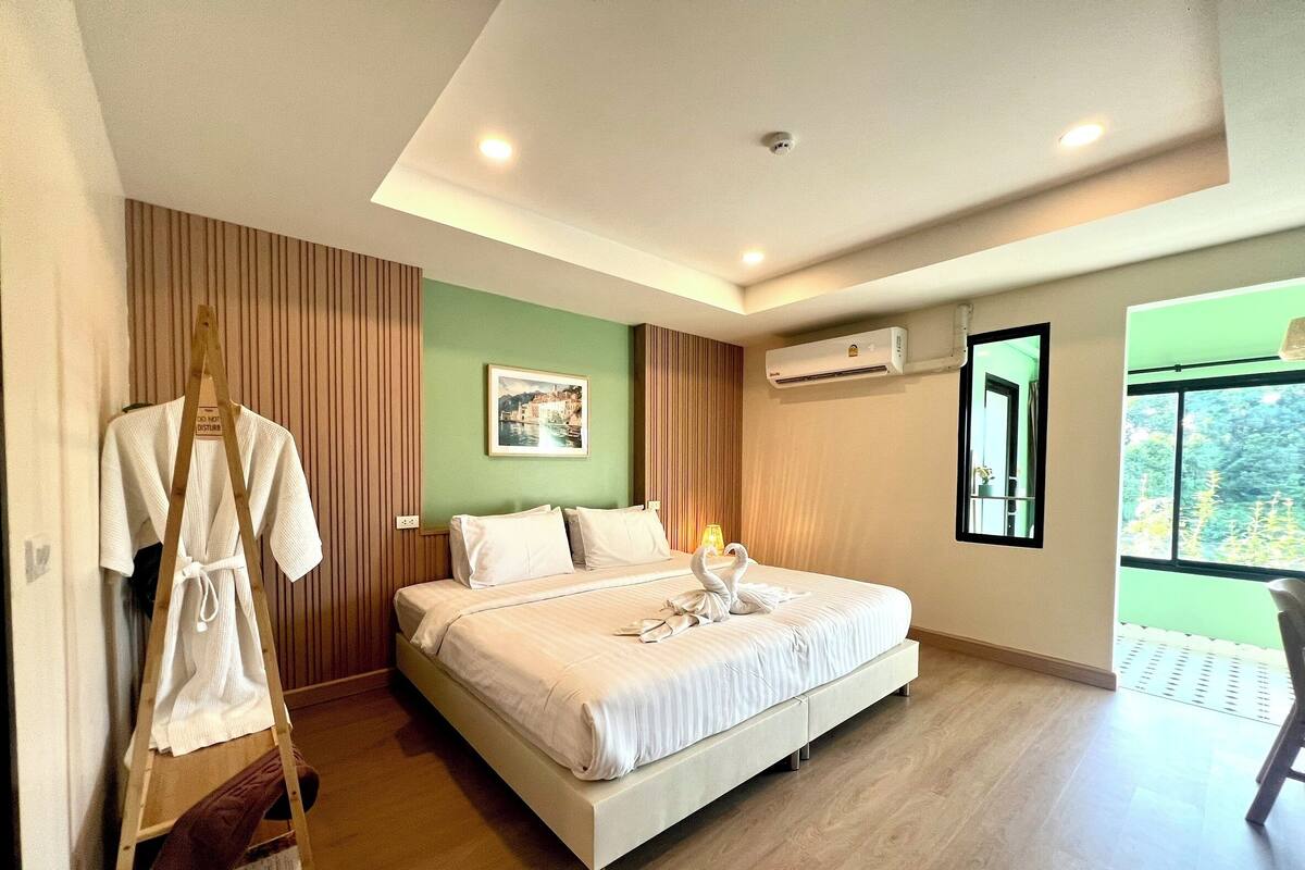 A neatly made bed with white linens, a wooden ladder, a framed picture on the wall, and an air conditioning unit.