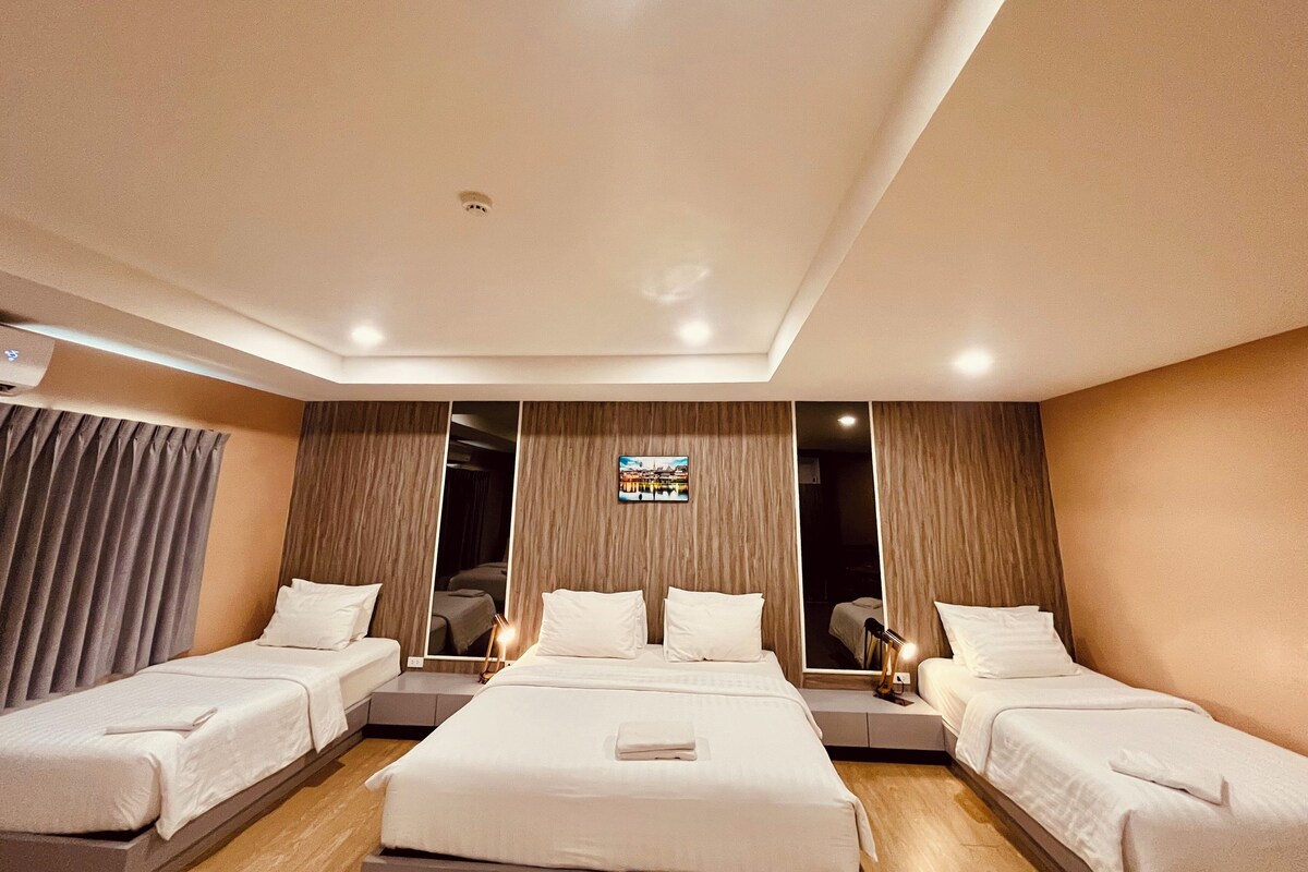 A hotel room with a large bed, two smaller beds, a mirror, and a view of the city.