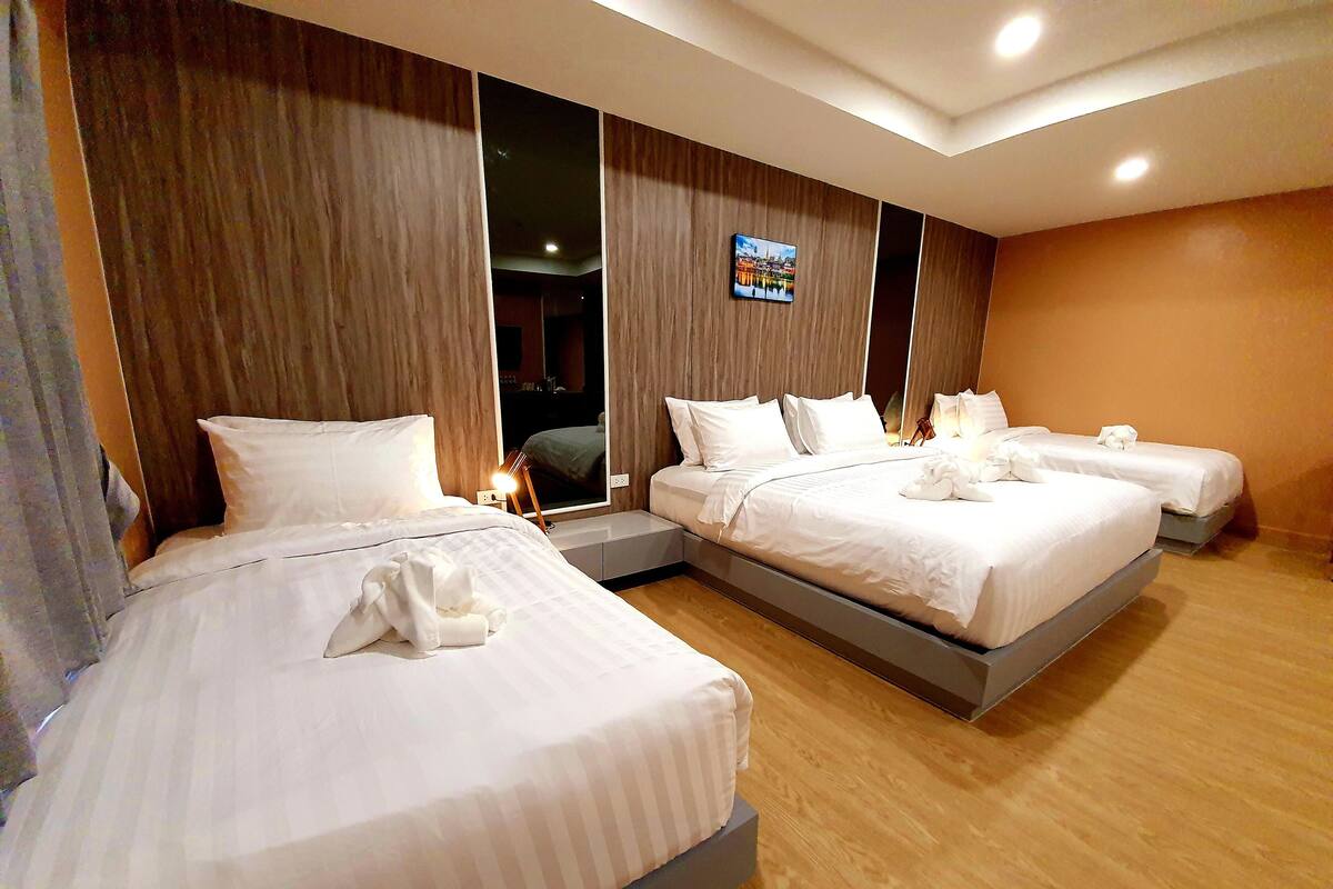 A hotel room with three beds, wooden flooring, and a large mirror.