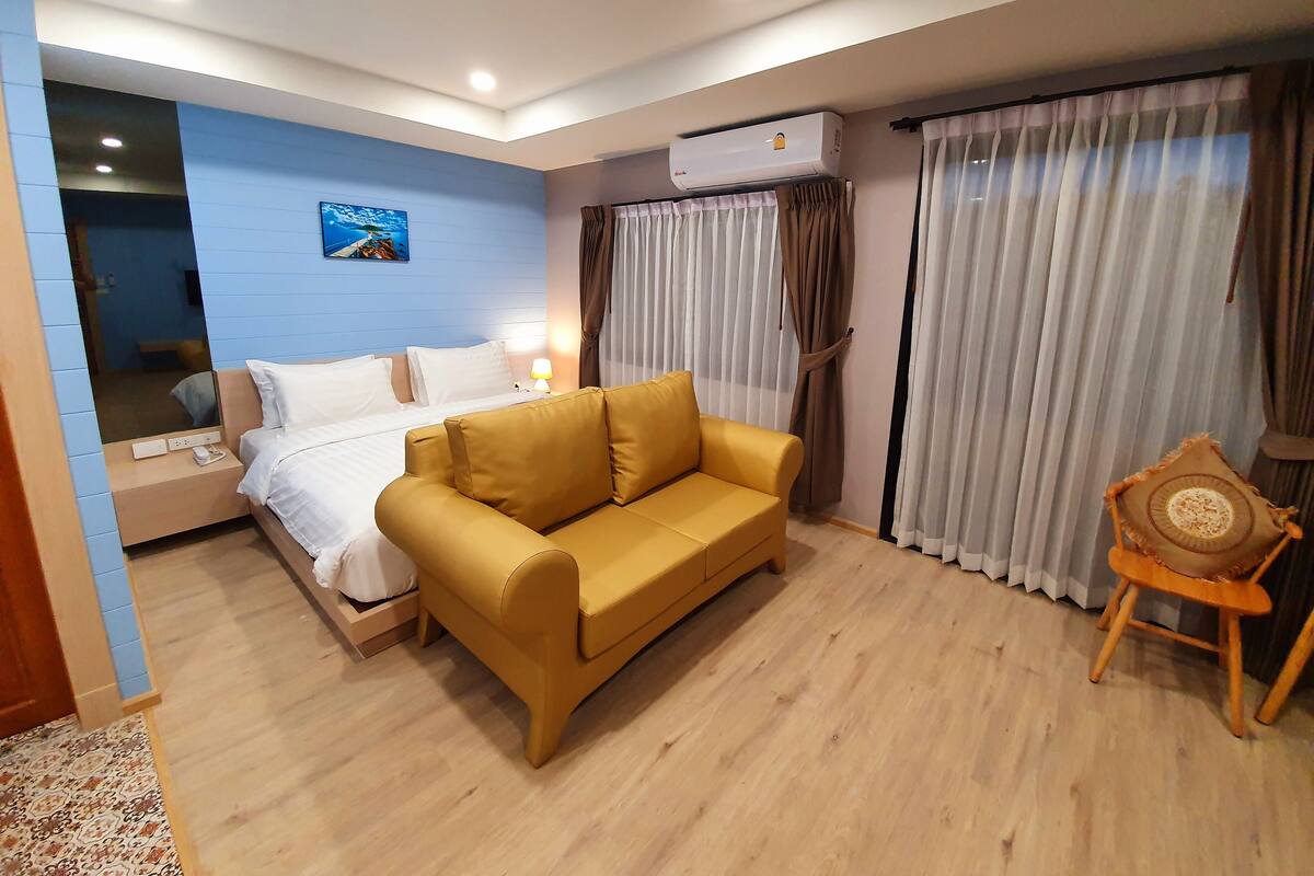A hotel room with a bed, a sofa, an air conditioning unit, and a window with curtains.