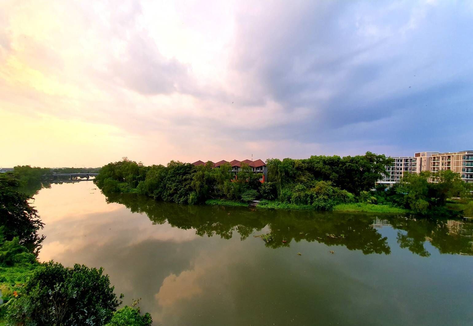Vista a la orilla del río con una hilera de edificios, incluyendo una casa con tejado rojo y un edificio de varios pisos con balcones.