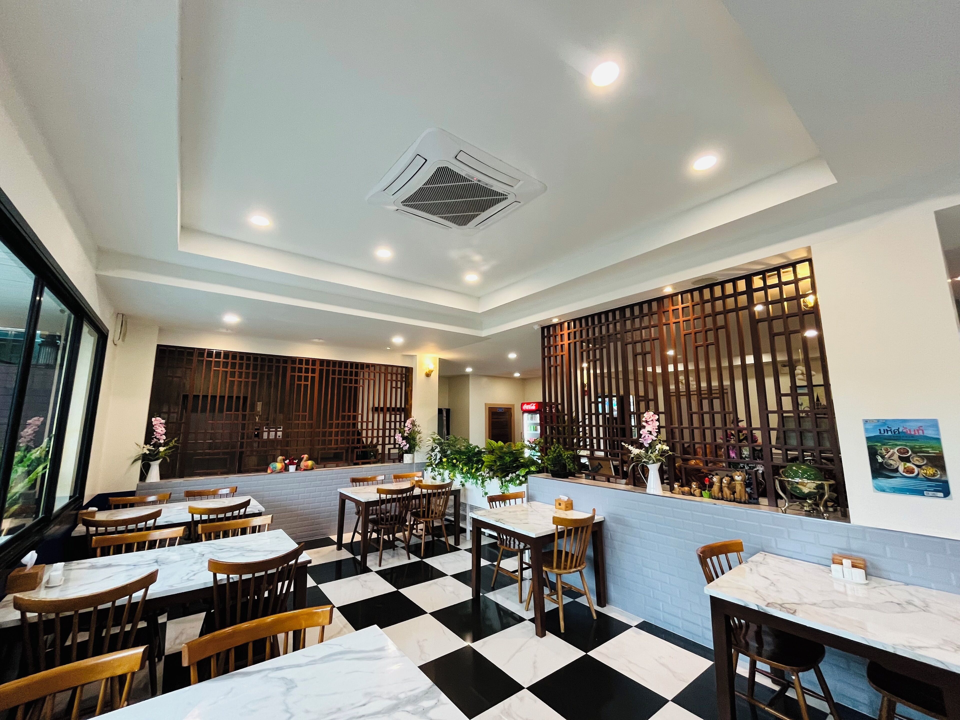 Un restaurante con suelo a cuadros, sillas de madera, mesas de mármol y un separador decorativo con plantas.
