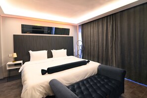 A modern hotel room with a large bed, a bedside table with a lamp, a black upholstered bench, and a dark curtain. - Via Çırağan Hotel (Istanbul)