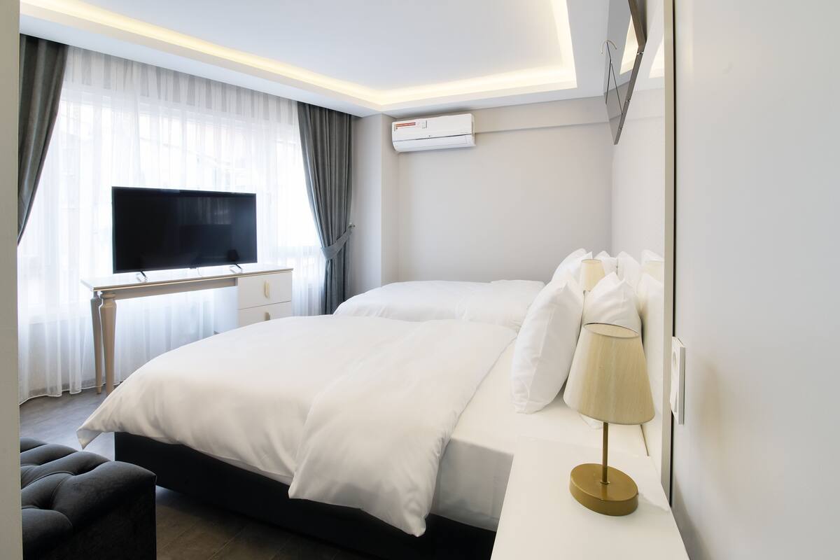 A modern hotel room with a large bed, a flat-screen TV, a desk, and an air conditioning unit.