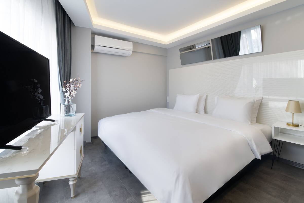 A modern hotel room with a large bed, a TV, a desk, and a mirror.