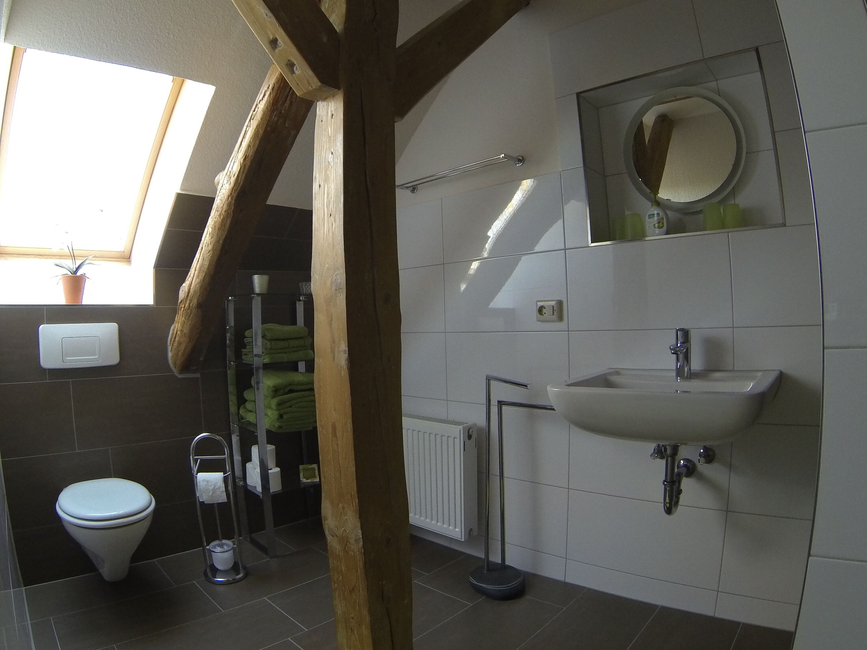 Et badeværelse med toilet, vask og håndklædestang. Der er et vindue med en plante, og en radiator er synlig.