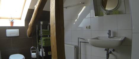 Et badeværelse med toilet, vask og håndklædestang. Der er et vindue med en plante, og en radiator er synlig.