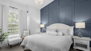 A bedroom with a large bed, two bedside tables with lamps, a bench, and a wall with a grid pattern.