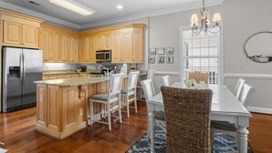 A kitchen with wooden cabinets, stainless steel appliances, a dining area with a white table and chairs, and a chandelier.