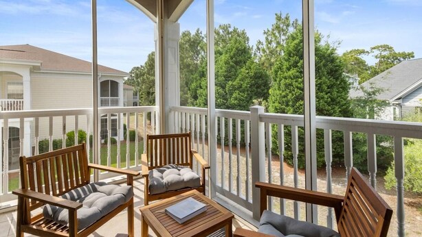 A covered outdoor area with wooden furniture, including chairs and a table, and a view of a residential neighborhood.
