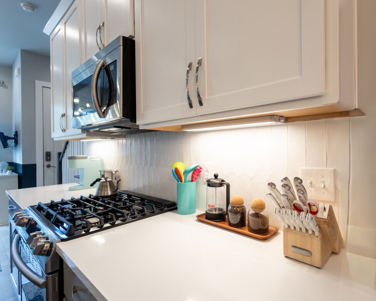A modern kitchen with white cabinets, a stainless steel stove, and a coffee maker on the counter.