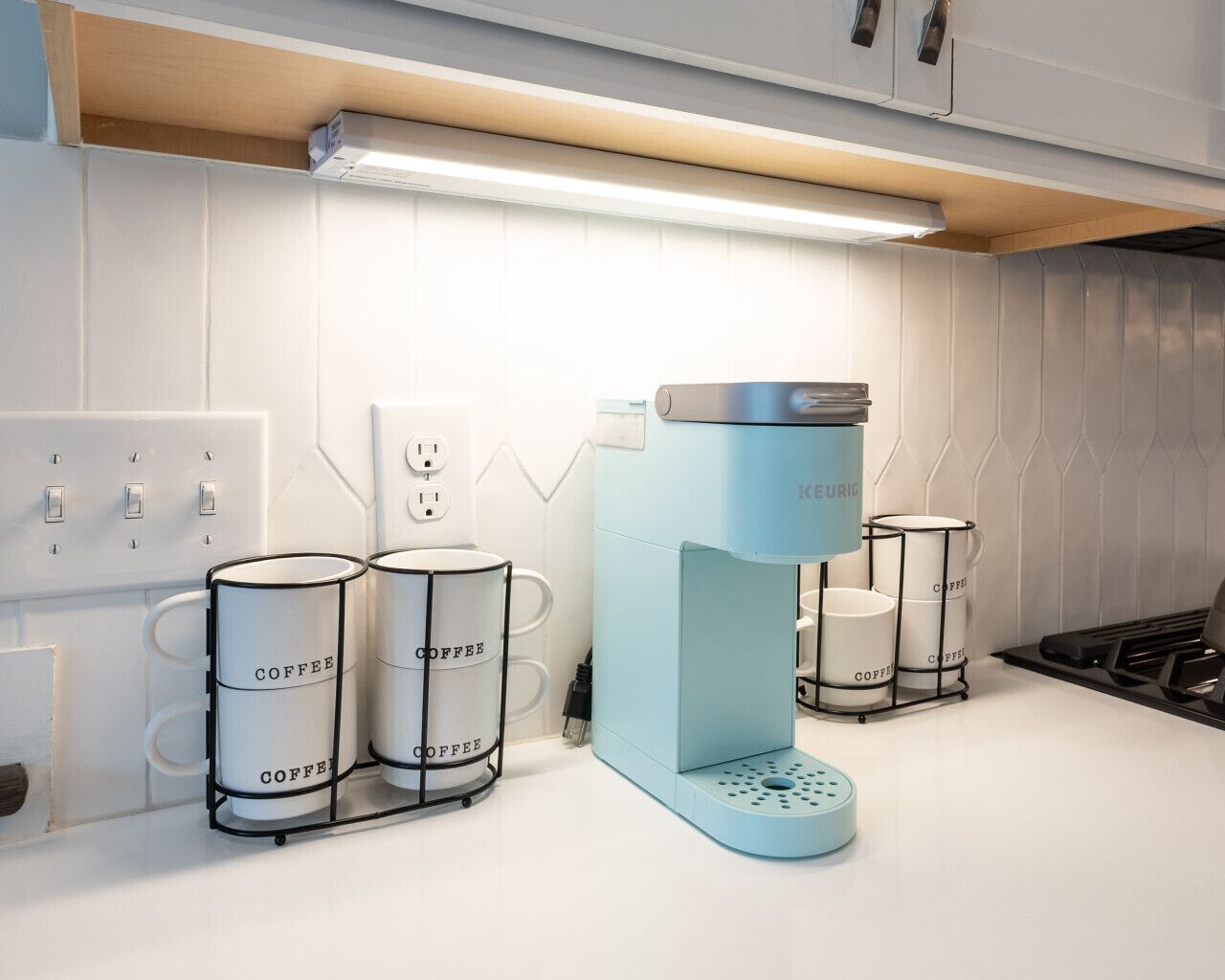 A kitchen with a coffee maker, two coffee dispensers, and a kettle.