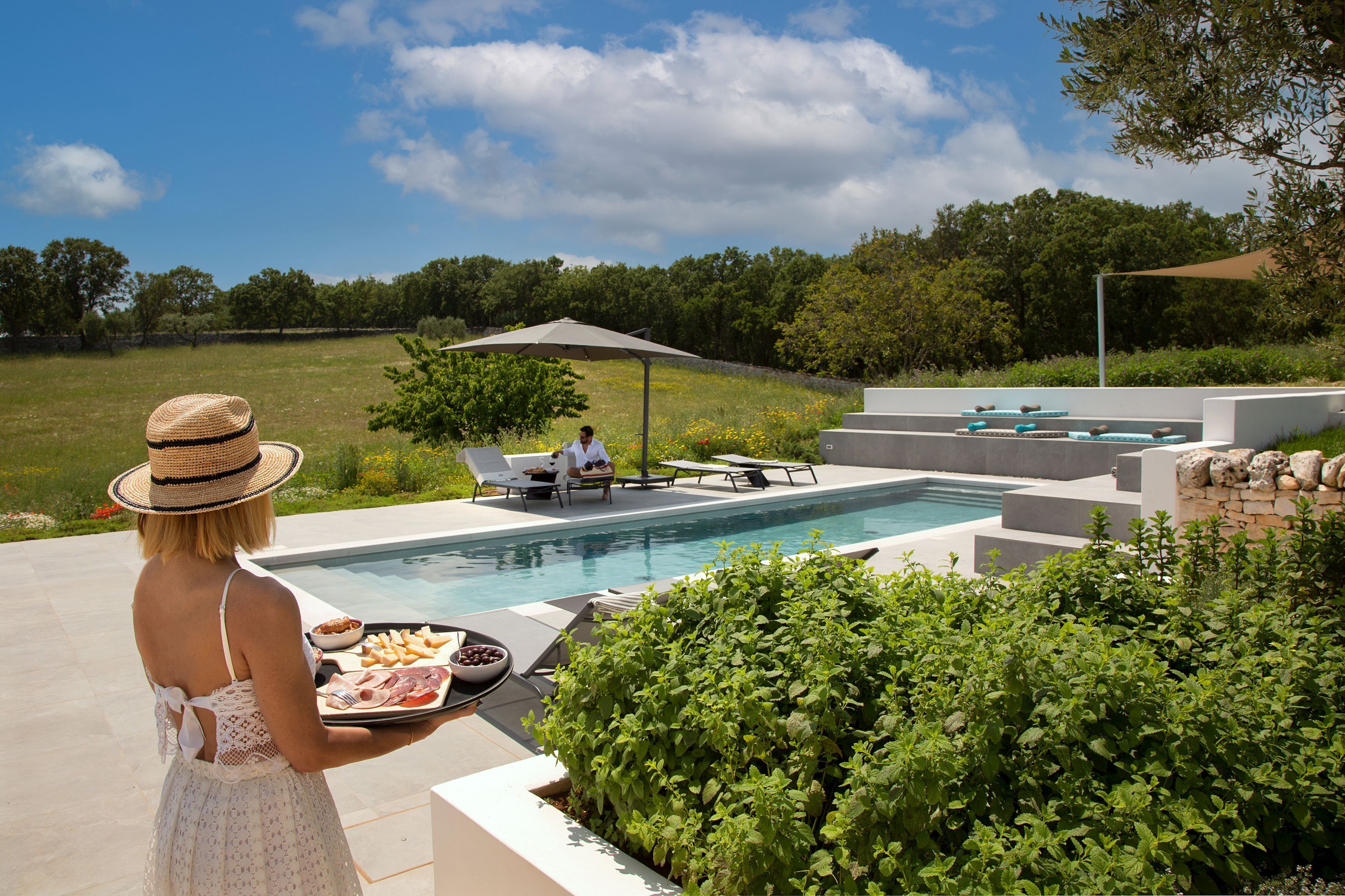Un espace aménagé au bord de la piscine, avec un coin repas, une chaise longue et une table où est assise une personne.