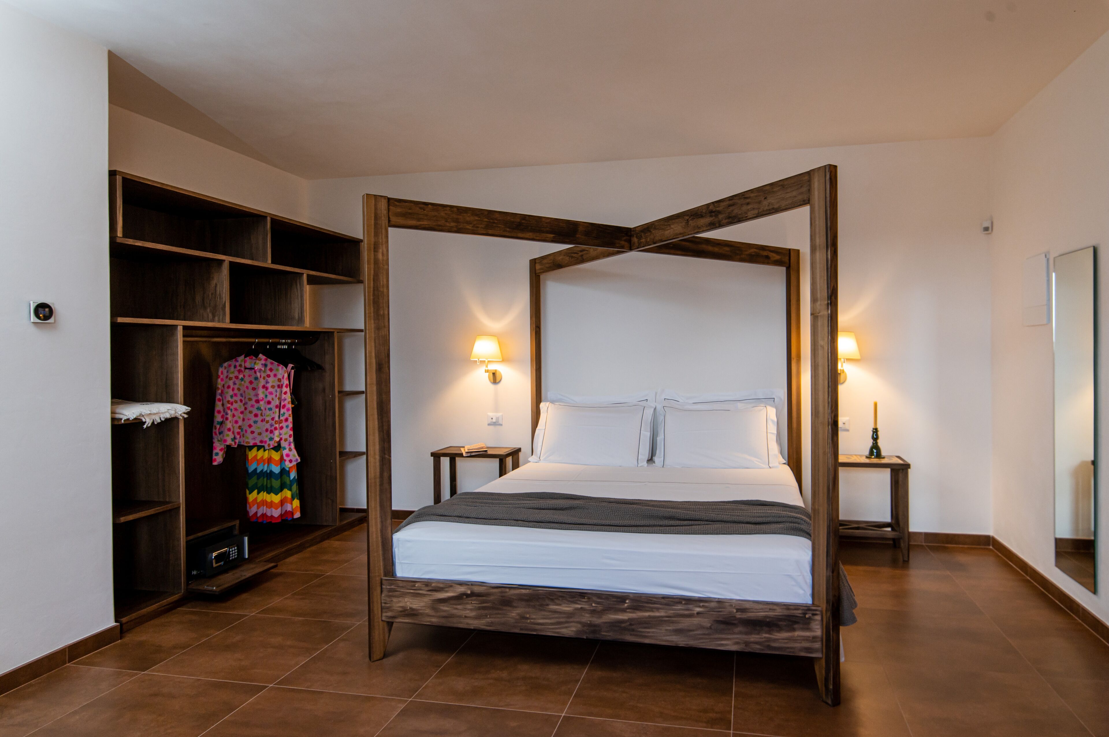 A four-poster bed with a wooden frame, a wardrobe with open shelves, and two bedside tables with lamps.