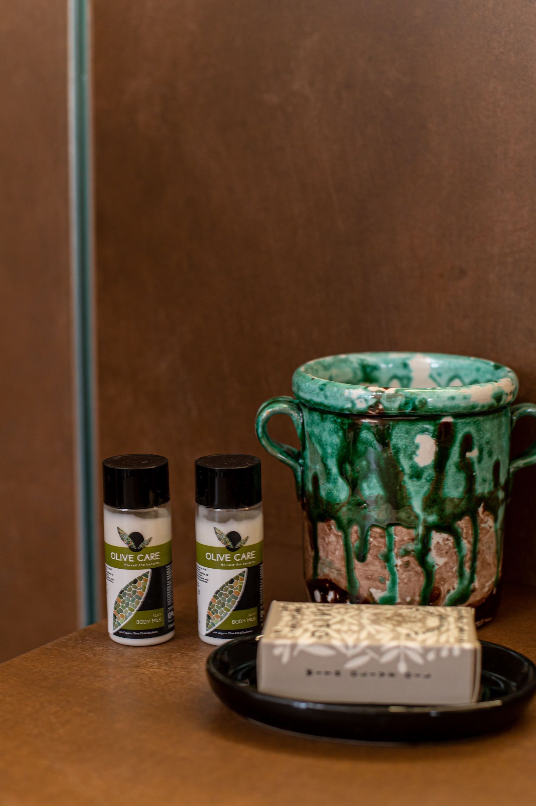 Una pequeña mesa con dos botellas de aceite de oliva, una taza decorativa y una pastilla de jabón.