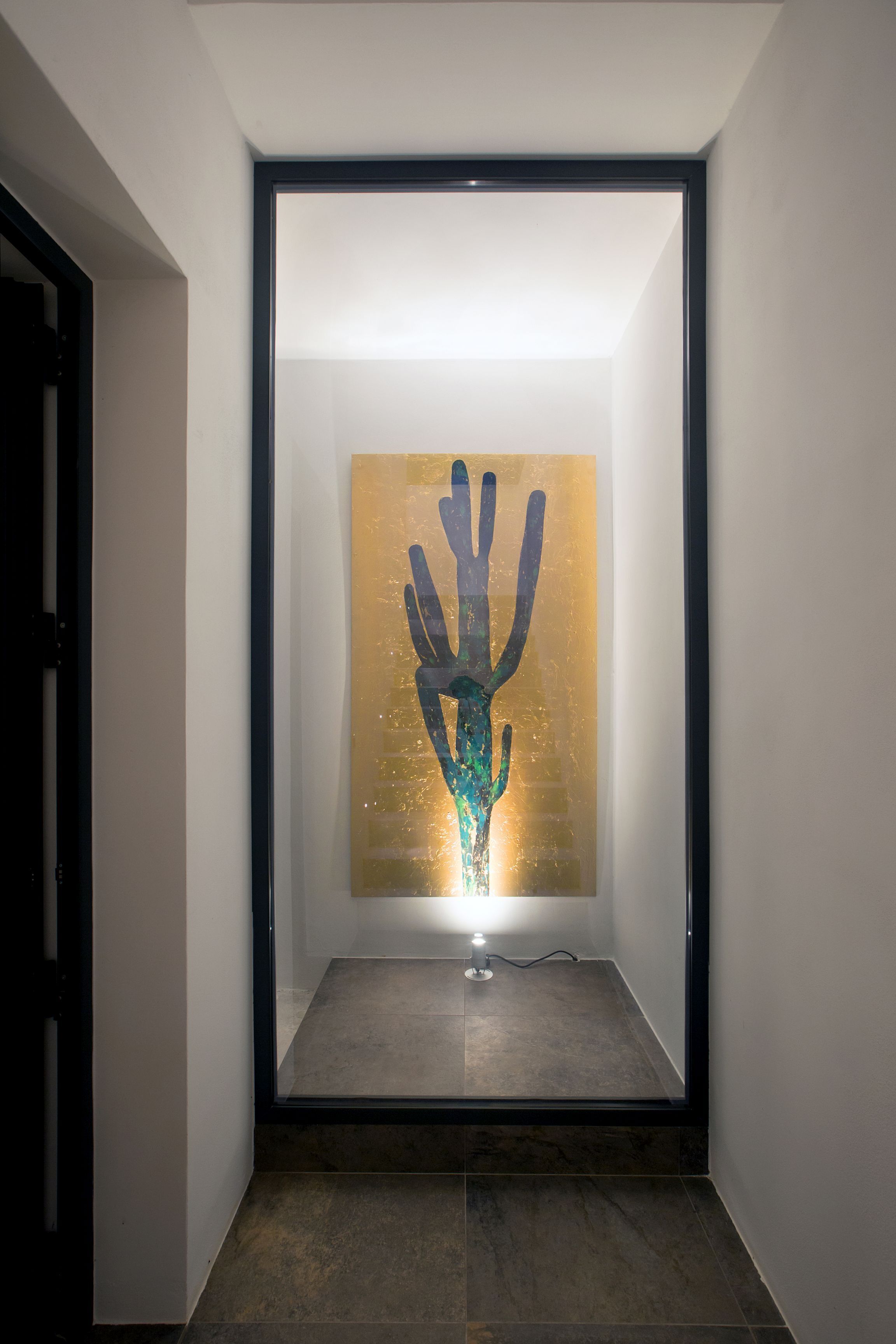 Un pasillo con una obra de arte moderna en la pared, una puerta a la izquierda y una lámpara en el suelo.