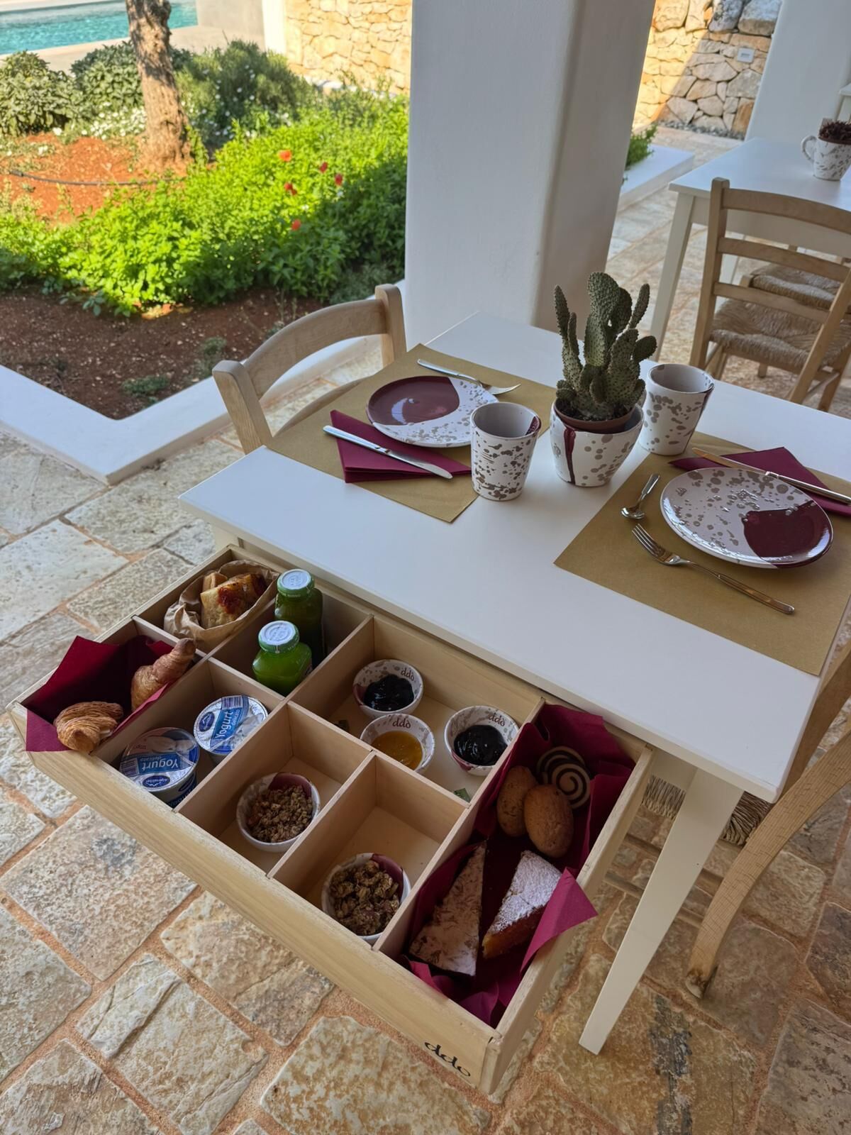 Une table à manger installée à l’extérieur, offrant une vue sur la verdure et un mur en pierre.