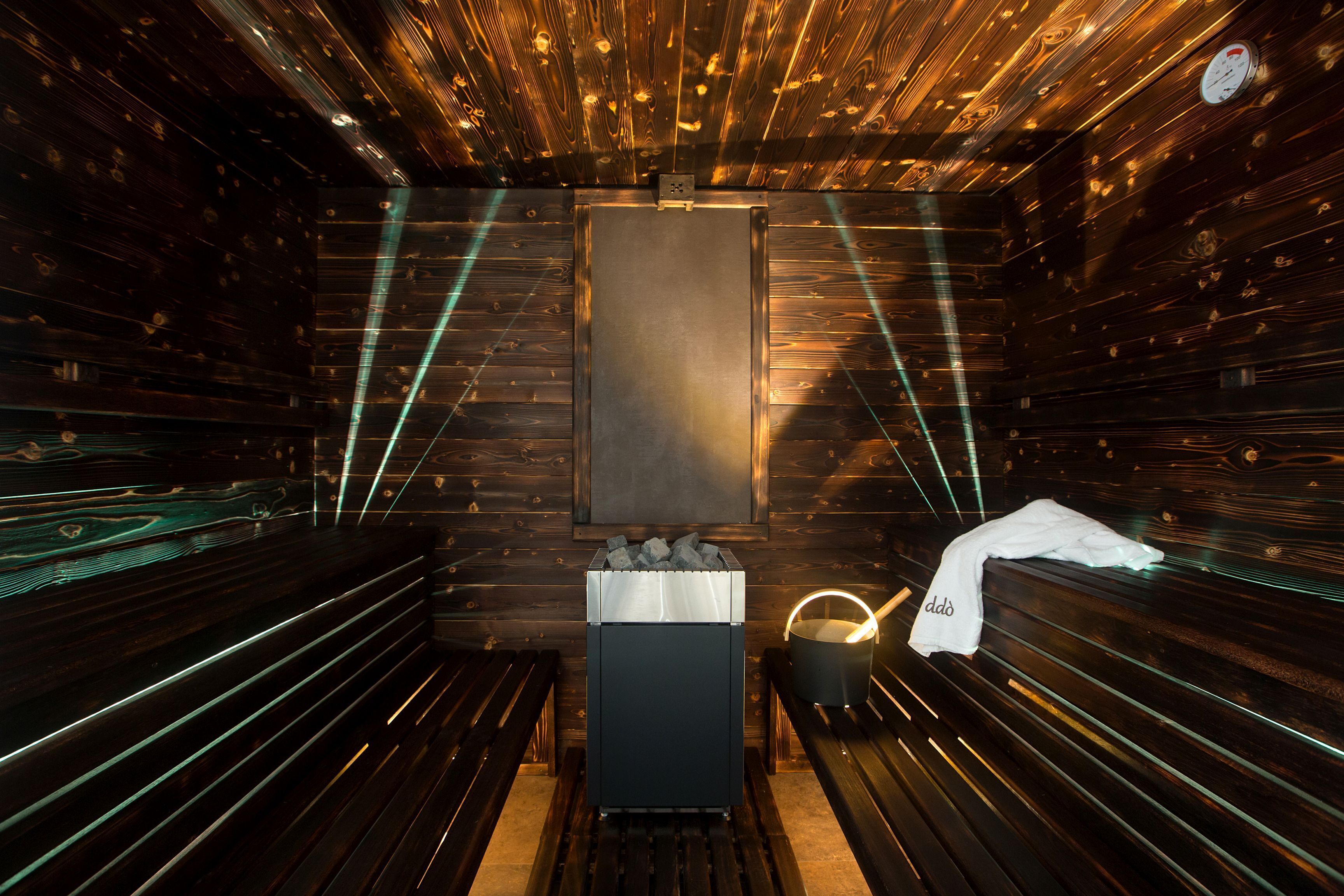 A sauna room with wooden walls, benches, a sauna heater, and a towel rack.