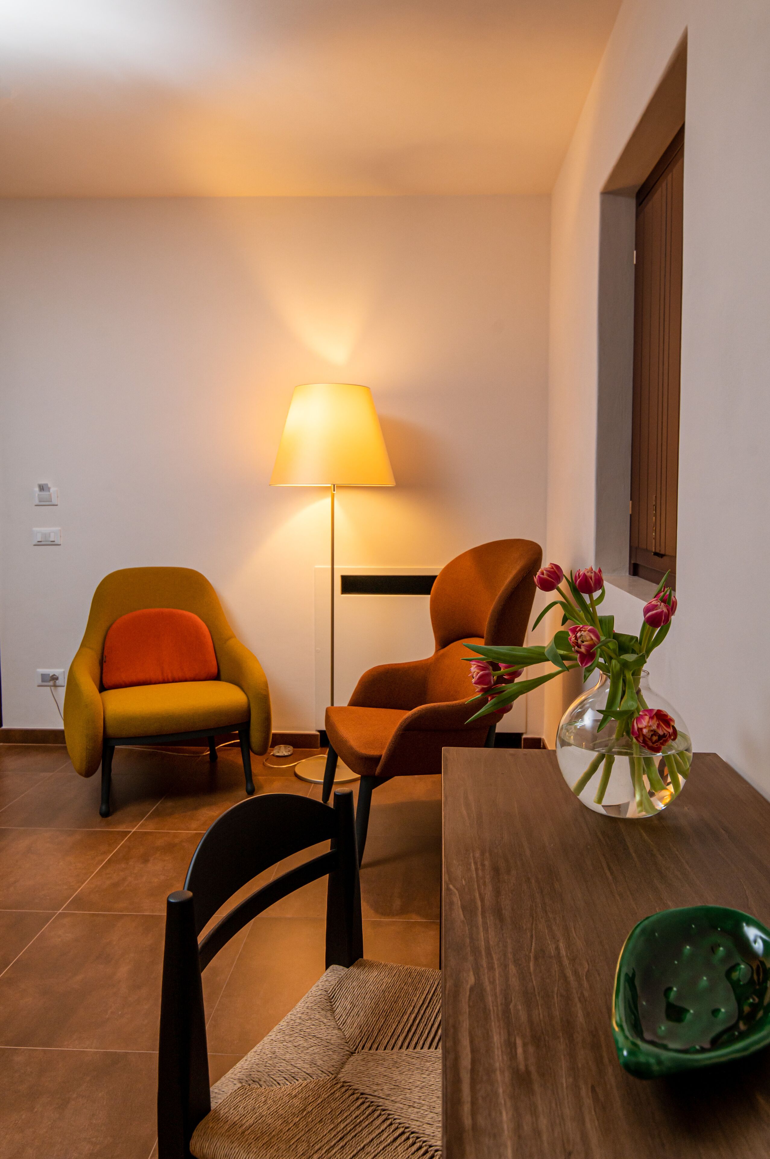 A modern living room with two armchairs, a floor lamp, a vase with flowers, and a wooden table.