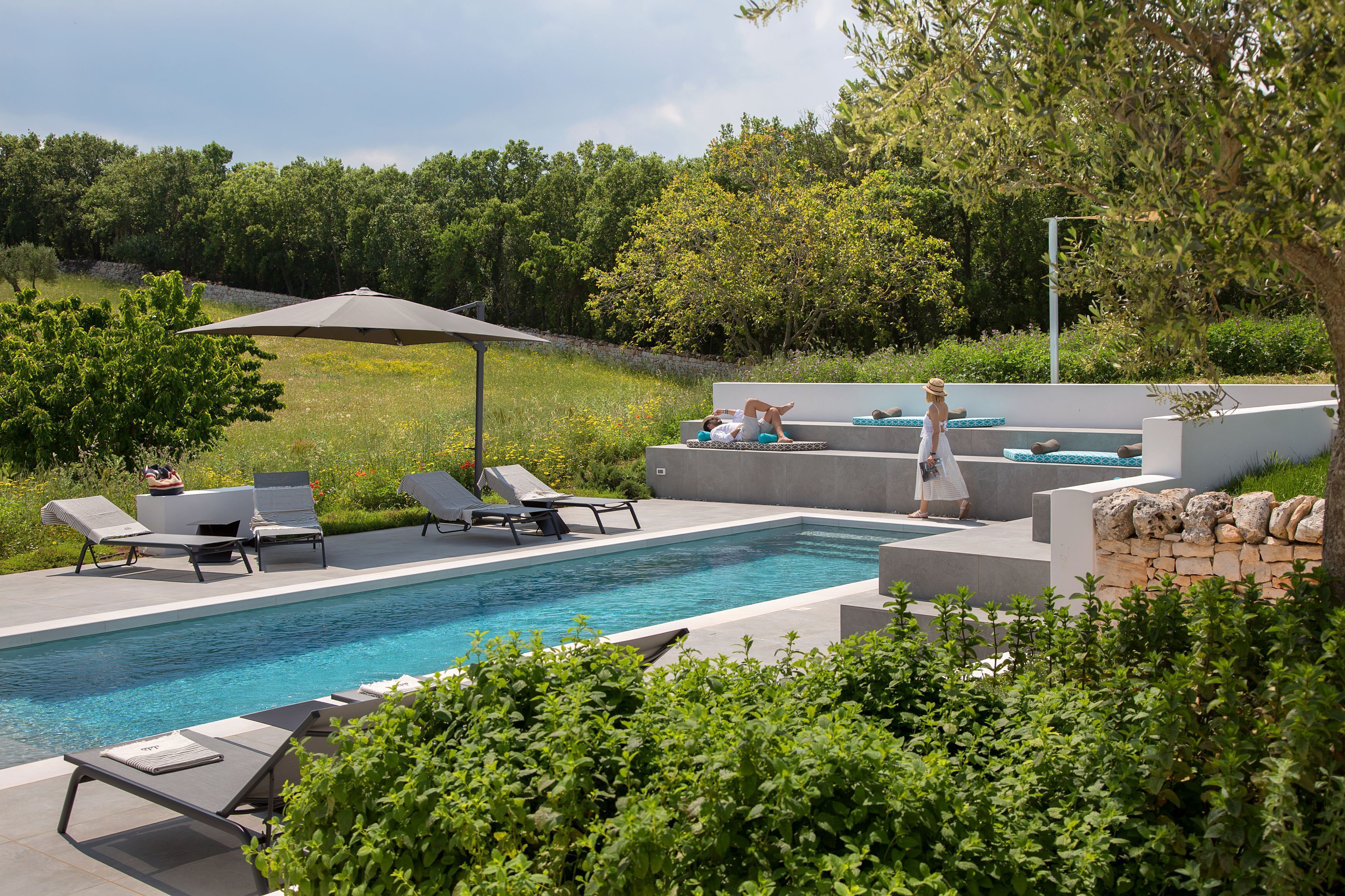 Un espace piscine extérieur moderne, doté de chaises longues, d’un jacuzzi et d’un mur en pierre.