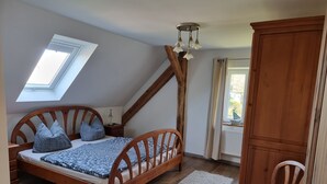 Ein Schlafzimmer mit schrägem Dach, einem hölzernen Bett mit Kopfteil, einem Dachfenster, einem Holzschrank und einem Fenster mit Vorhängen.