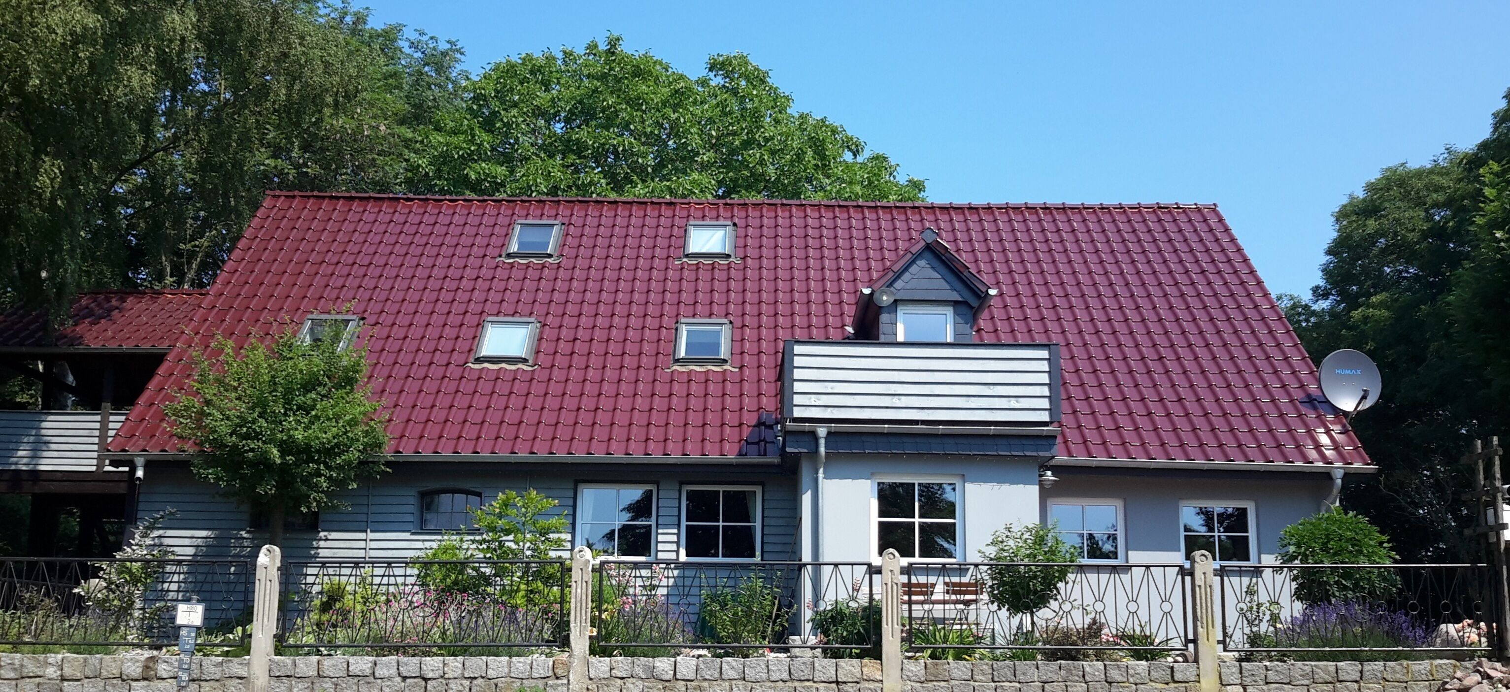 A two-story house with a red-tiled roof, multiple windows, and a satellite dish.