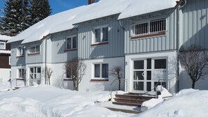 Un bâtiment à deux étages, dont le toit est recouvert de neige, et des marches qui mènent à l’entrée.