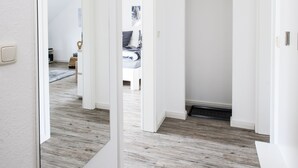 Un couloir doté d’un plancher en bois, de murs blancs et d’un grand miroir sur le côté gauche.