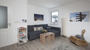 Un salon moderne avec un canapé gris, une table basse en bois, une bibliothèque et un panneau décoratif fixé au mur.