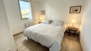 A bedroom with a large bed, two bedside lamps, a window with curtains, and a picture on the wall.
