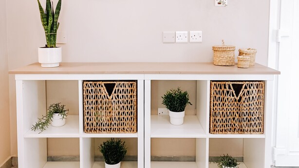 Une console blanche agrémentée de paniers tressés, d’un miroir et de plantes en pot.