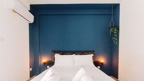 Un lit bien fait, avec du linge de lit et des serviettes blanches, une tête de lit bleu foncé et des lampes fixées au mur.