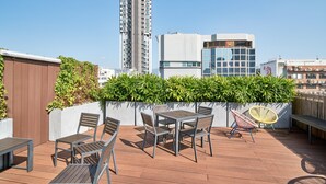 A rooftop terrace with outdoor furniture, a view of a tall building, and a modern building with large windows. - Weave Studios - Prince Edward (Kowloon)
