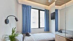 A modern bedroom with a bed, bedside table, potted plant, and a desk with a chair. - Weave Studios - Prince Edward (Kowloon)