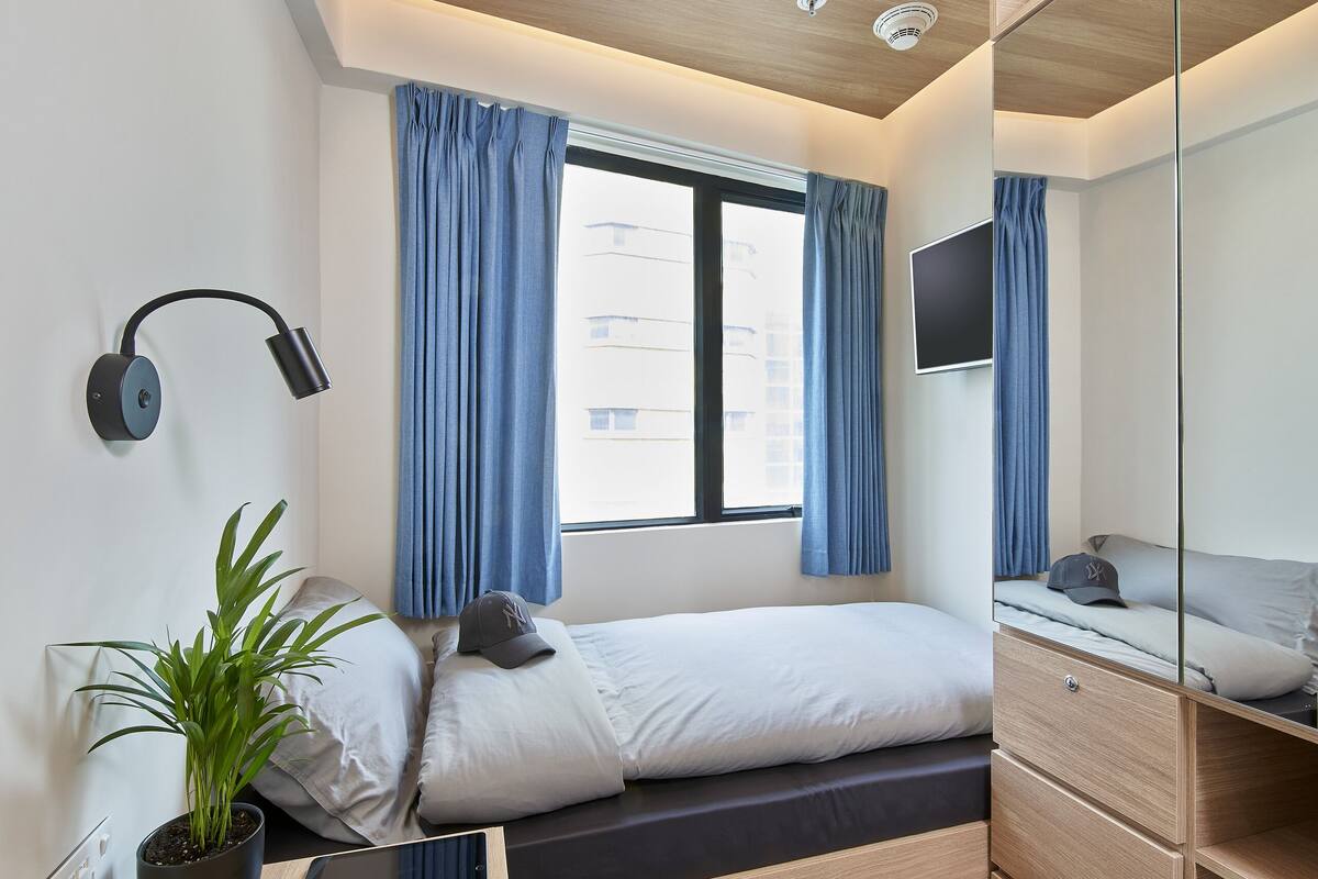A modern bedroom with a bed, bedside table, potted plant, and a desk with a chair.