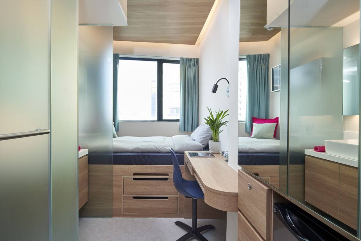 A compact bedroom with a bed, desk, chair, and a potted plant.