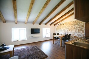 A modern kitchen with wooden beams, stone wall, and a dining area with a TV above the table.