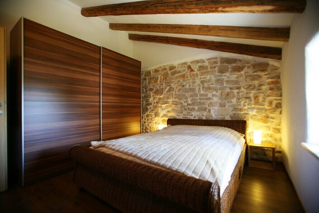 A bedroom with a stone wall, wooden beams, a bed, and a wardrobe.