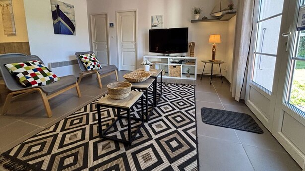 Una sala de estar con televisor, sofá, alfombra estampada y ventana con vistas.
