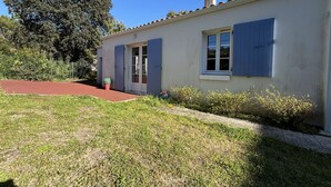 Edificio de una sola planta con un sendero rojo que lleva a la entrada, un pequeño jardín con una planta en maceta y un cielo azul despejado.
