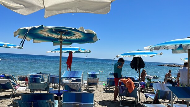 A beach with rows of blue lounge chairs and white umbrellas.
