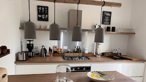 A modern kitchen with a wooden countertop, a gas stove, a coffee maker, and a glass of water.