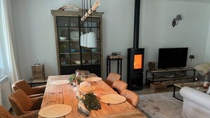 A dining area with a wooden table, cushioned chairs, a glass-top centerpiece, and a black wood-burning stove.